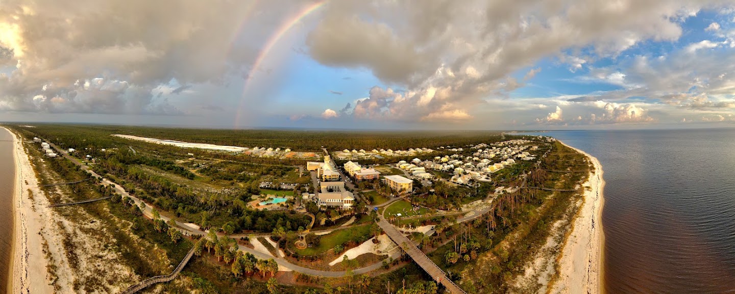 Wide aerial panorama of a coastal property beneath a rainbow